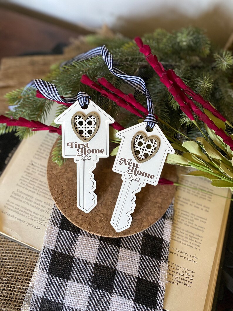 May include: Two wooden key-shaped ornaments with a house design and a heart cutout. The top ornament says "First Home 2022" and the bottom ornament says "New Home 2022".