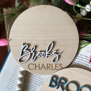 May include: Two round wooden signs with the names "Brooks Charles" and "Brooks" in white and teal lettering.
