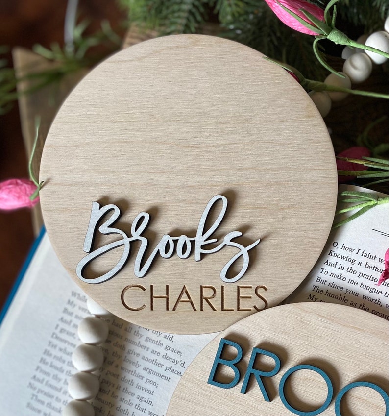 May include: Two round wooden signs with the names "Brooks Charles" and "Brooks" in white and teal lettering.