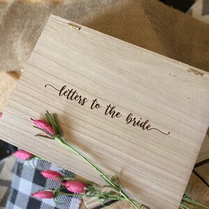 Puede incluir: Una caja de madera con las palabras "cartas para la novia" grabadas en la tapa. La caja est&aacute; decorada con una rama de flores rosas.