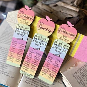 May include: Three colorful wooden bookmarks shaped like apples with the text "Thank you for being a part of our story!" and the teacher's name. Each bookmark has a list of student names.