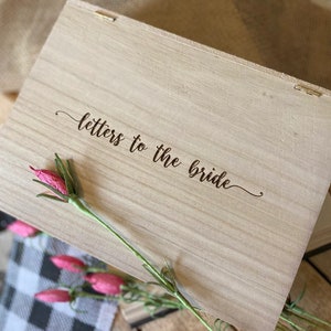 Puede incluir: Una caja de madera con las palabras "cartas para la novia" grabadas en la tapa. La caja est&aacute; decorada con una flor rosa.