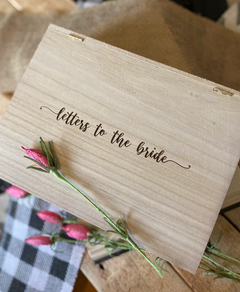 Puede incluir: Una caja de madera con las palabras "cartas para la novia" grabadas en la tapa. La caja est&aacute; decorada con una flor rosa.