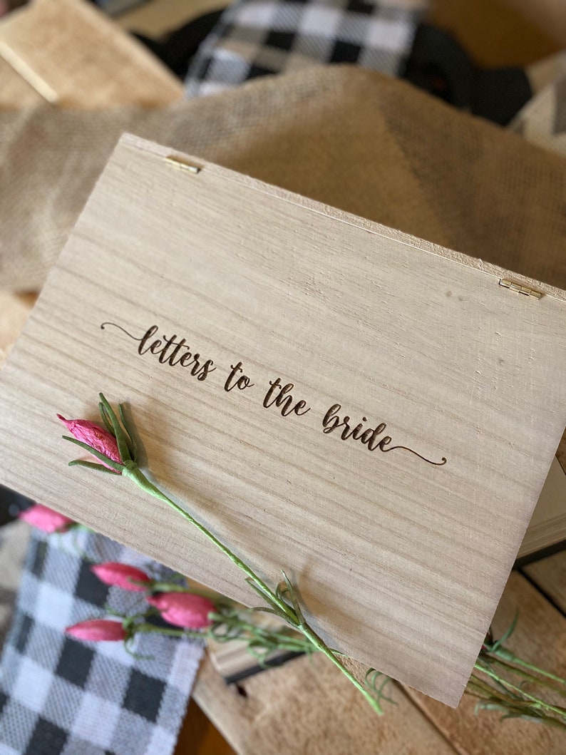 Puede incluir: Una caja de madera con las palabras "letters to the bride" grabadas en la tapa. La caja est&aacute; decorada con una flor rosa.