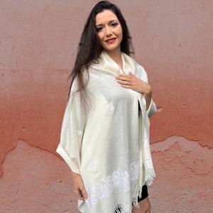 May include: A white shawl with delicate embroidery. The shawl is made of a soft, lightweight fabric and has a fringed edge.