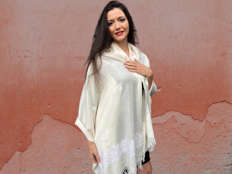 May include: A white shawl with delicate embroidery. The shawl is made of a soft, lightweight fabric and has a fringed edge.
