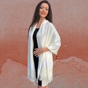 May include: A white shawl with delicate embroidery and fringe. The shawl is made of a soft, lightweight fabric and is perfect for adding a touch of elegance to any outfit.