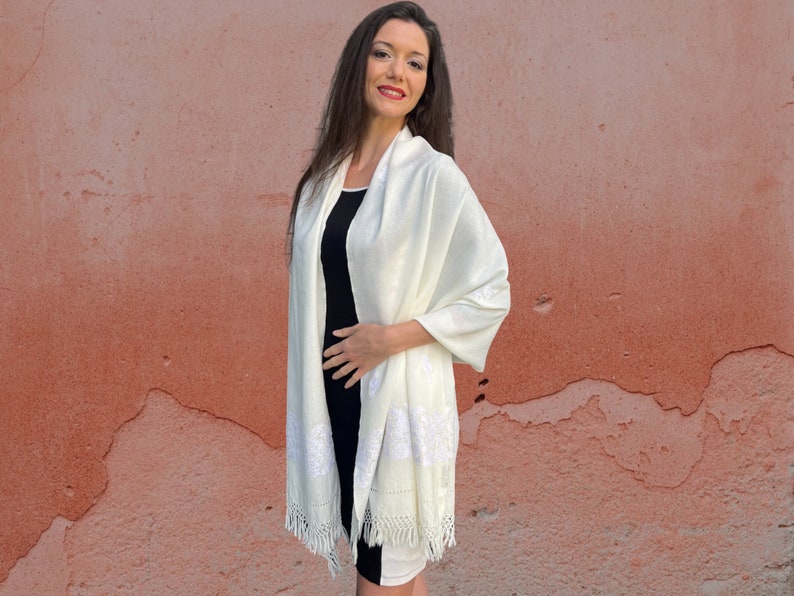 May include: A white shawl with delicate embroidery and fringe. The shawl is made of a soft, lightweight fabric and is perfect for adding a touch of elegance to any outfit.