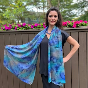 May include: A blue and brown patterned scarf with a fringed edge. The scarf is draped around a person's neck and shoulders.