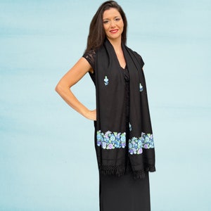 May include: A black shawl with a floral design in shades of blue and green. The shawl has a fringe border and is made of a soft, lightweight fabric.