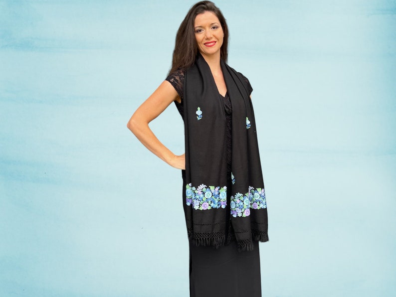 May include: A black shawl with a floral design in shades of blue and green. The shawl has a fringe border and is made of a soft, lightweight fabric.