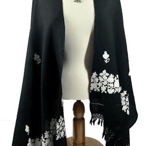 May include: Black shawl with white floral embroidery and fringe. The shawl is draped over a mannequin and has a silver pendant necklace.