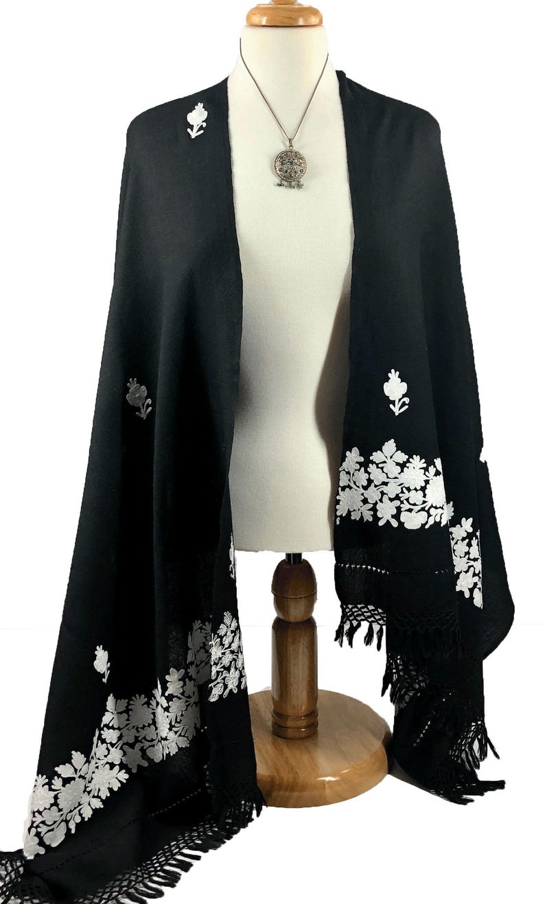 May include: Black shawl with white floral embroidery and fringe. The shawl is draped over a mannequin and has a silver pendant necklace.
