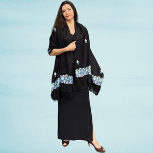 May include: A black shawl with a floral design in shades of blue and purple. The shawl has a fringe border and is draped over a person's shoulders.