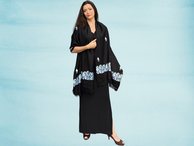 May include: A black shawl with a floral design in shades of blue and purple. The shawl has a fringe border and is draped over a person's shoulders.