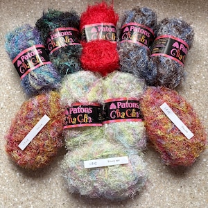 May include: A collection of Patons Cha Cha yarn skeins in various colors, including red, blue, green, and multi-colored blends. Some skeins have labels that read "Salsa" and "Bonny Hop".