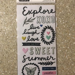 May include: A package of puffy stickers with summer-themed phrases and images. The stickers include the words "Explore," "XOXO," "Live, Laugh, Love," and "Sweet Summer." There are also heart and butterfly designs.