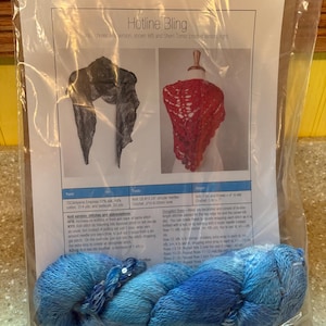 May include: A package containing a knitting pattern titled "Hotline Bling" with a blue and white yarn skein. The pattern includes images of a scarf and a top, along with yarn and tool specifications.