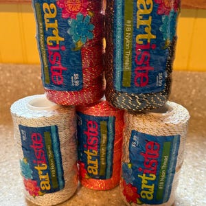 May include: A collection of spools of Artiste #18 Nylon Thread in various colors, including red, silver, orange, and dark blue. Each spool has a blue label with floral designs and the text "artiste". The price tag reads $6.99.