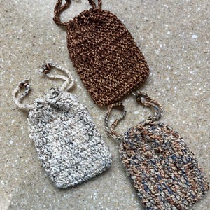 May include: Three small rectangular crochet pouches with drawstring closures. One pouch is solid dark brown, one is a speckled off-white, and one features a variegated blend of brown, blue, and tan yarn. Each pouch has two matching beaded drawstrings.