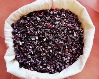 May include: A white cloth bag filled with dried, dark purple berries.