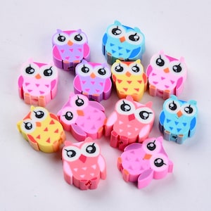 May include: A set of 12 colourful owl-shaped beads. The beads are made of plastic and have a hole in the centre for stringing. The owls are in various colours, including pink, purple, blue, and yellow.