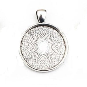 May include: A circular silver-toned metal pendant tray featuring a raised bail at the top. The interior of the pendant base displays a detailed, repeating geometric pattern of small, interlocking diamond shapes radiating from the center.