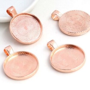 May include: Four circular rose gold pendant trays with a textured, cross-hatched pattern inside the base. Each pendant tray features a smooth, raised rim and a small, integrated bail at the top for attaching to a necklace or jewelry chain.