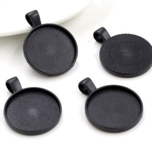 May include: Four circular black pendant trays with a textured interior base and a top loop for hanging. These jewelry findings feature a matte black finish and a recessed center designed for setting cabochons or other decorative elements.