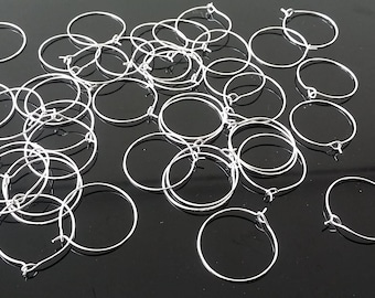 May include: A pile of silver hoop earrings, all of the same size and style, are scattered on a black surface.