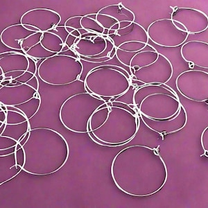 May include: A large group of silver hoop earrings on a purple background. The hoops are all the same size and are arranged in a random pattern.