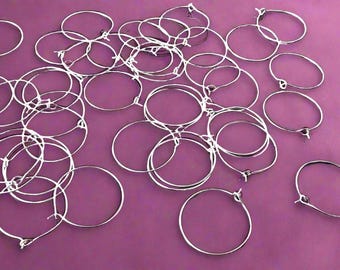 May include: A large group of silver hoop earrings on a purple background. The hoops are all the same size and are arranged in a random pattern.