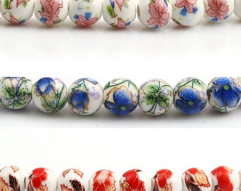 May include: Three rows of white ceramic beads with floral patterns. The top row has pink flowers, the middle row has blue flowers, and the bottom row has red flowers.