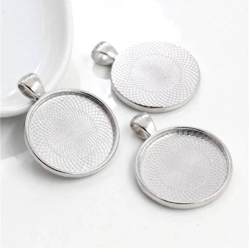 May include: Three silver-toned circular pendant trays with a smooth, raised outer rim and a textured, geometric pattern on the interior base. Each pendant features a small, integrated bail at the top for attachment to a chain or cord.