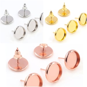 May include: Three pairs of earring settings, each pair in a different color: silver, gold, and rose gold. Each setting has a round, flat base with a small hole in the center for attaching a post. The settings are designed to hold a round, flat cabochon.