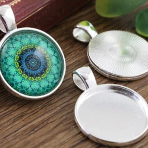 May include: Three circular silver-toned pendants with a bail at the top. One pendant features a vibrant green, blue, and yellow mandala-style pattern under a glass dome, while the other two are empty silver-toned metal settings with smooth interiors.