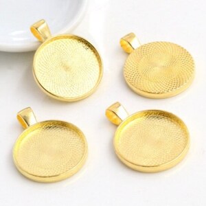 May include: Four gold-colored circular pendant trays with a textured interior pattern and a small bail at the top. Each pendant base features a smooth outer rim and a flat, recessed center designed for holding small decorative inserts or cabochons.