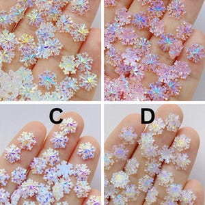 May include: Four sets of iridescent snowflake embellishments, each held in a hand. The sets display different colour palettes: clear, pink, white, and a mix of clear and white. Each snowflake is approximately 1 cm.