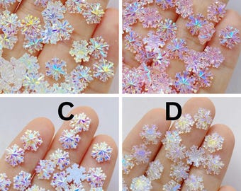 May include: Close-up of four sets of iridescent snowflake-shaped embellishments. Each set is held in a hand and features a different color palette: clear, pink, white, and a mix of clear and white.