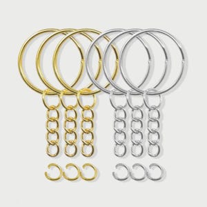 May include: A selection of gold and silver keychains. The keyrings have large circular hoops, chain links, and small C-shaped rings. The gold keyrings have a bright, shiny finish, while the silver ones have a cool, metallic appearance.