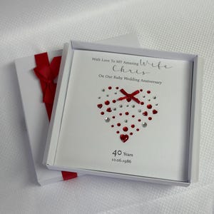 May include: A square white greeting card in a matching box with a red ribbon. The card features the text With Love To MY Amazing Wife Chris On Our Ruby Wedding Anniversary, a heart made of red and clear crystals, and 40 Years 10.06.1986.