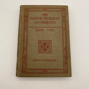 May include: An antique book titled "The Silver-Burdett Arithmetics Book Two." The cover is a muted green with a red border and text. The book's title and publisher, Philips & Anderson, are displayed prominently.