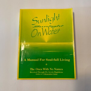 May include: A yellow and green book titled "Sunlight On Water: A Manual For Soul-full Living" by Flo Aeveia Magdalena, author of "I Remember Union".