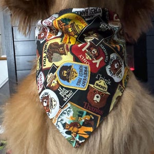 May include: A black bandana featuring Smokey Bear and forest fire prevention messages. The bandana has a repeating pattern of Smokey Bear patches with text like "Prevent Forest Fires" and "Only You". The bandana is worn by a dog.