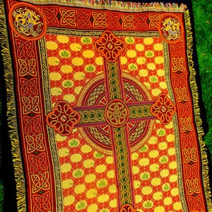 May include: A woven throw blanket featuring a prominent Celtic cross design in red, orange, and yellow. The background displays a repeating grid pattern with small green shamrocks. The border includes intricate knotwork and corner medallions.
