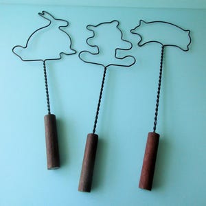 May include: Three vintage wire shadow puppets with wooden handles. The puppets are shaped like a rabbit, a bear, and a pig.