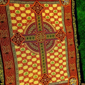 May include: A woven throw blanket featuring a large central Celtic cross design in red, gold, and green. The background has a repeating lattice pattern with small green shamrocks. The border displays intricate knotwork and corner medallions.
