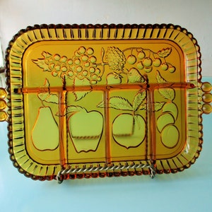 May include: Amber glass divided serving tray with a raised fruit design. The tray has four sections and features grapes, strawberries, pears, apples, and peaches.