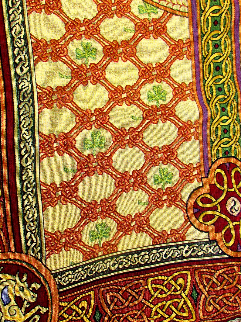 May include: A woven textile featuring a cream-colored background with an orange lattice pattern and small green shamrocks. The border displays intricate knotwork in shades of red, green, and yellow, with a stylized animal figure in the corner.