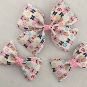 May include: Three pink and white hair bows with a nutcracker pattern. The bows are made of ribbon and have pink polka dot centers.